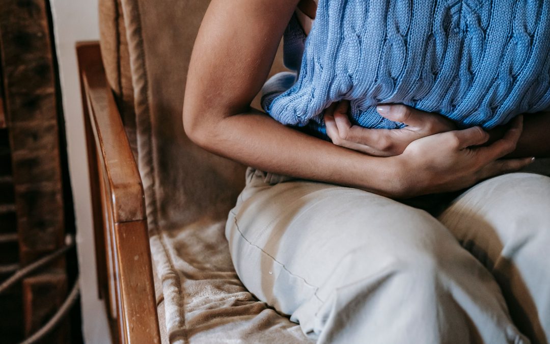 Woman sitting on a couch holding a pillow to her stomach in discomfort